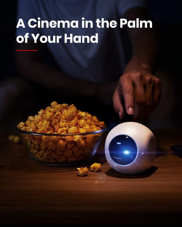 A man points to a Nebula Astro portable projector sitting on a table next to a bowl filled with caramel corn.