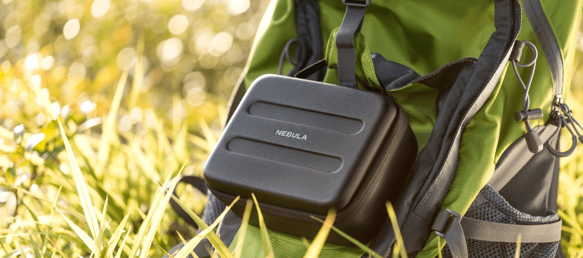 A Capsule Carry Case is strapped to the back of a backpack laying on the grass.